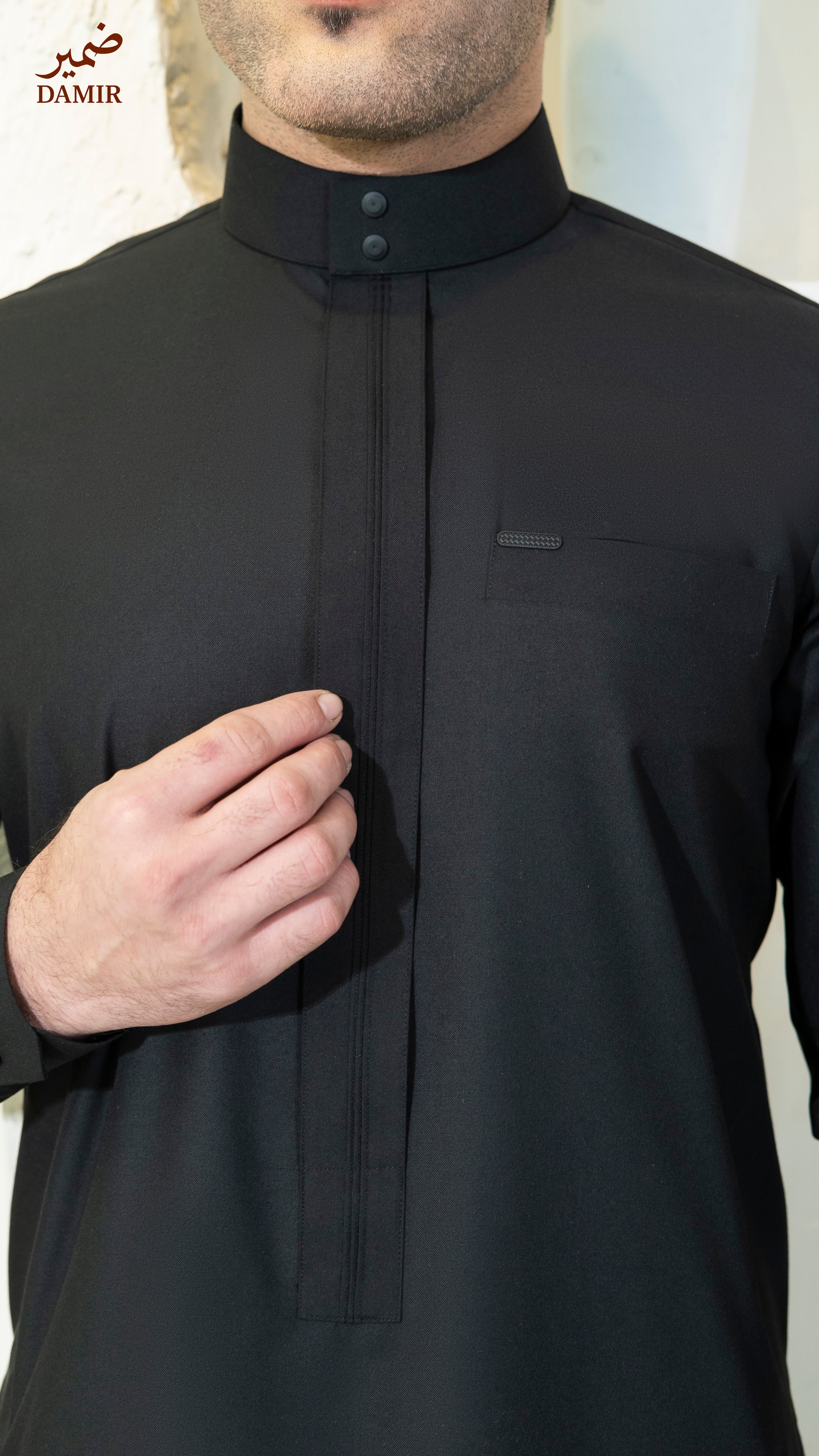 Black traditional outfit with a collar, worn by a person, on a plain background.