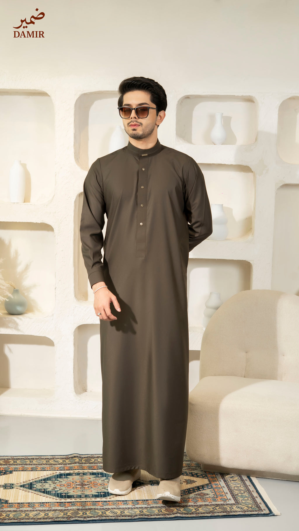 Man wearing a long dark brown garment in a modern interior setting