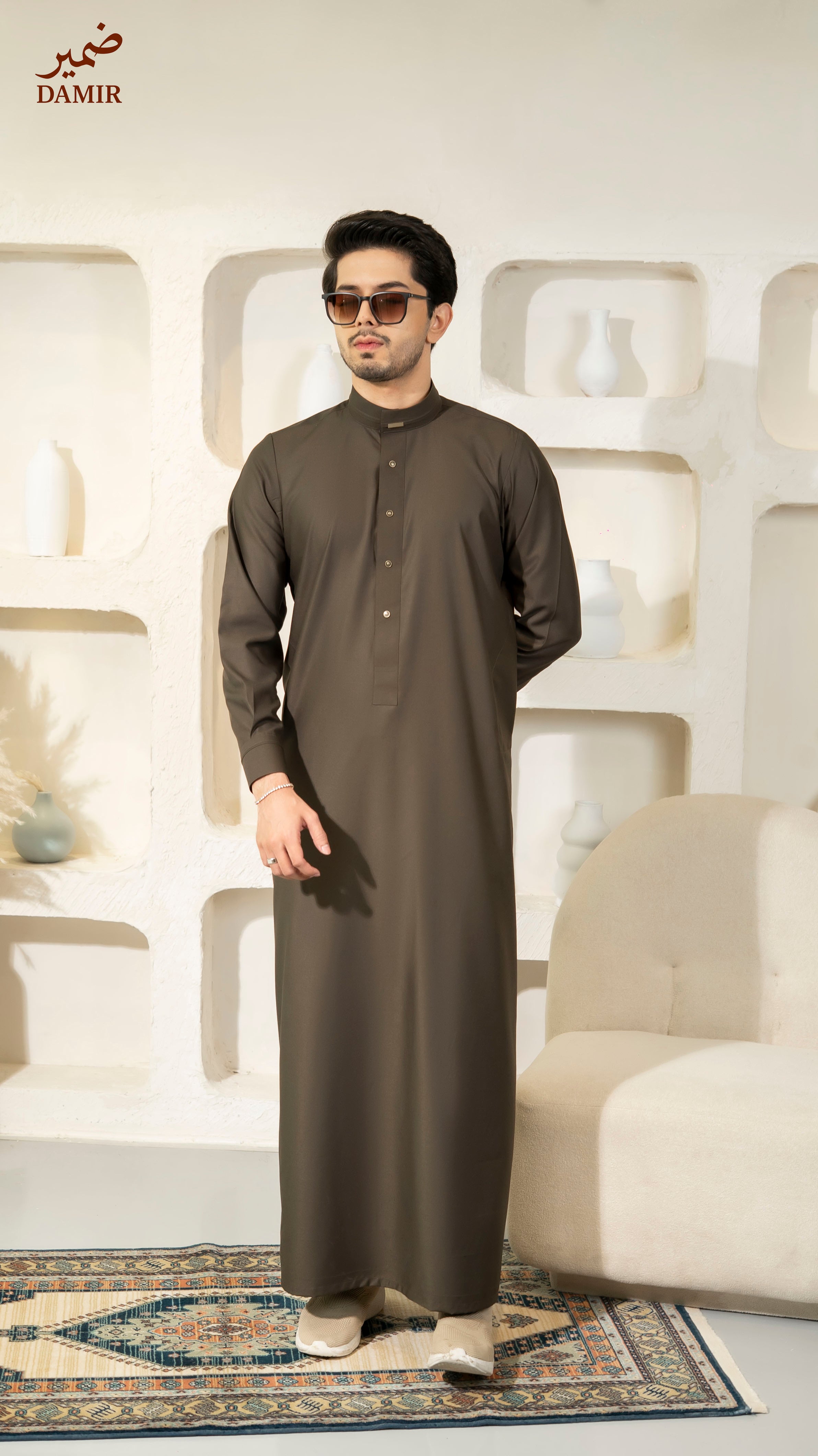 Man wearing a long dark brown garment in a modern interior setting