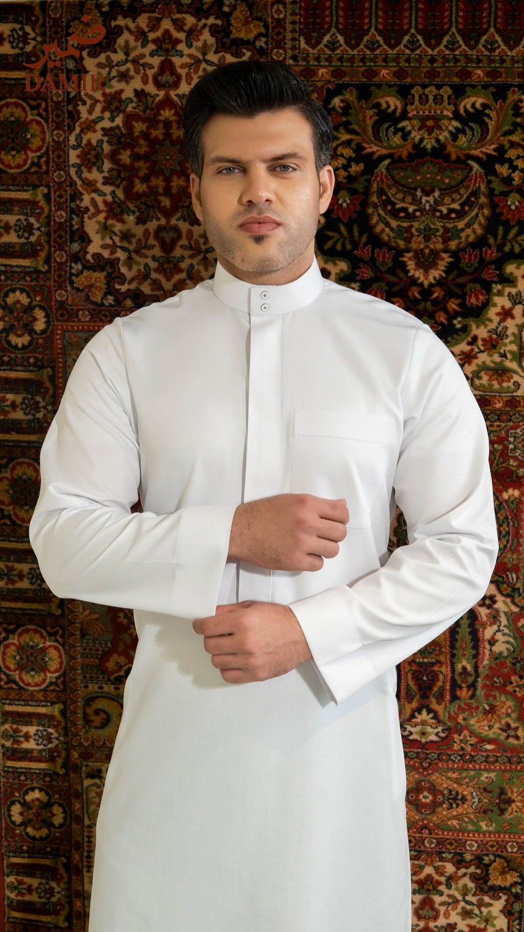 Man wearing a white traditional outfit against a patterned rug background
