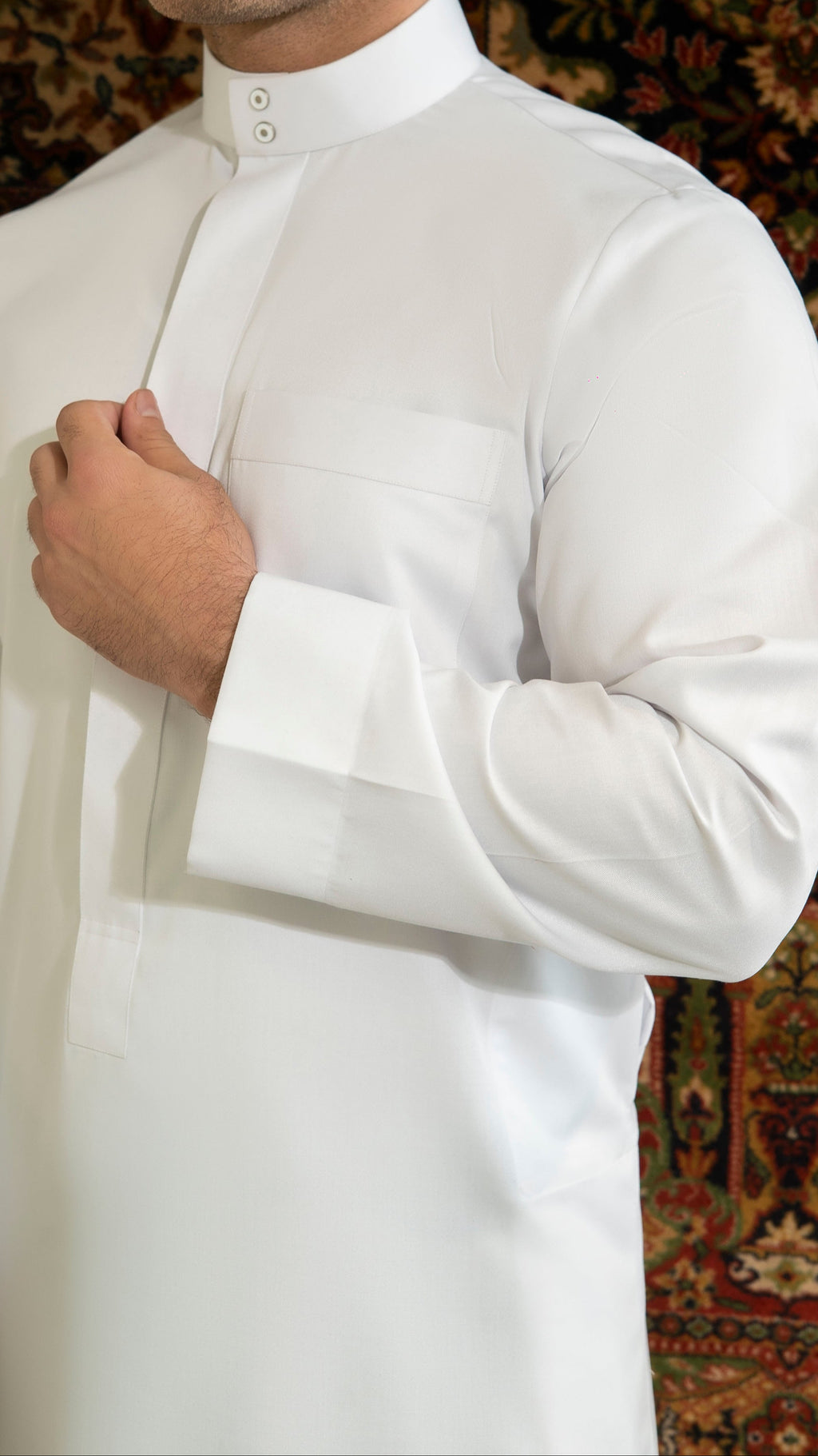 Man wearing a white traditional outfit against a patterned rug background